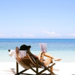 Woman sitting on a beach reading a book in a beach chair, enjoying a holiday showing one way to use a personal loan.